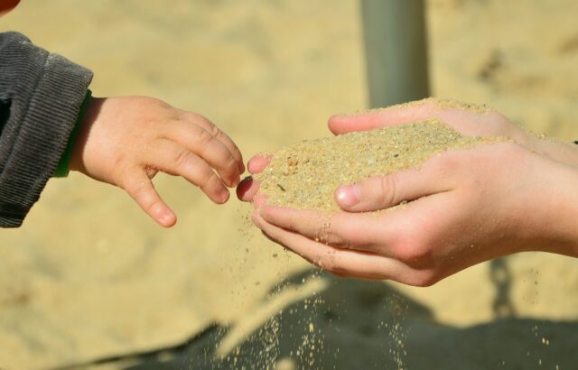 ręce trzymające przesypujące się przez palce piasek
